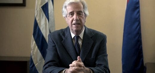 alt="tabaré vázquez en primer plano, detrás una bandera de Uruguay"