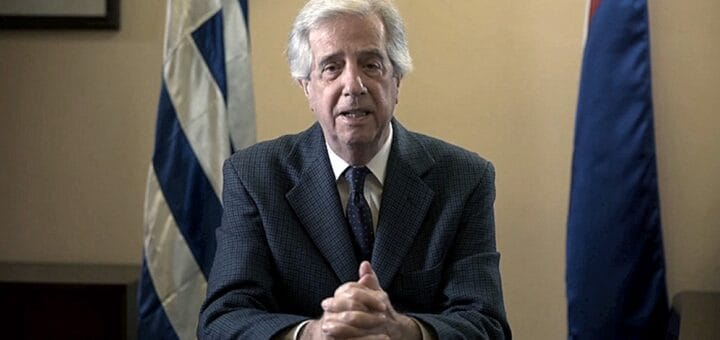 alt="tabaré vázquez en primer plano, detrás una bandera de Uruguay"