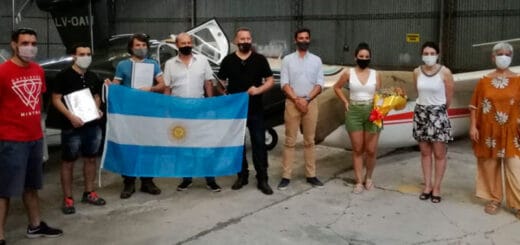 alt="nueve personas con una bandera argentina paradas delante de un avión"