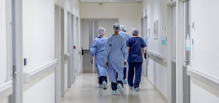 alt="enfermeros de espaldas caminando por un pasillo"