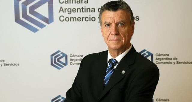 alt="natalio mario grinman posa ante un cartel de la cámara argentina de comercio y servicios"