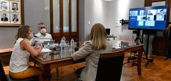 alt="en una cabecera de una mesa la vicegobernadora Laura Stratta, de espaldas la ministra Rosario Romero; sentado de frente el fiscal de Estado, Julio Rodriguez Signes. Todos ante un monitor, durante una videoconferencia"