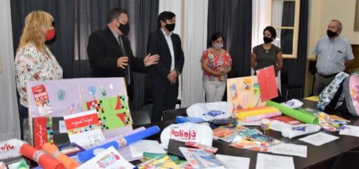 alt="en la imagen, en una mesa se exhiben distintos artículos escolares, detrás el intendente y comerciantes"