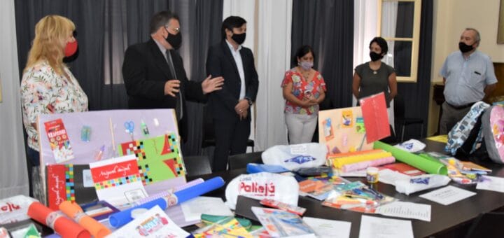 alt="en la imagen, en una mesa se exhiben distintos artículos escolares, detrás el intendente y comerciantes"