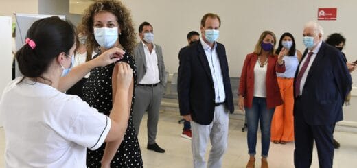 alt="en esta imagen, en primer plano se ve a una mujer recibiendo una vacuna, más atrás el gobernador Bordet y el ministro González García, luego algunos funcionarios"