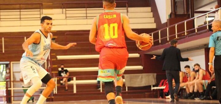 alt="un jugador de tomás de rocamora avanza haciendo picar la pelota ante otro de racing de chivilcoy"