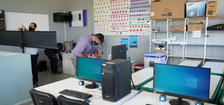 alt="dos mesas con pantallas de computadoras y un CPU, hombres instalando equipamiento tecnológico"