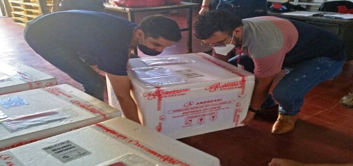 alt="dos personas descargan contenedores de la vacuna Sputnik V"