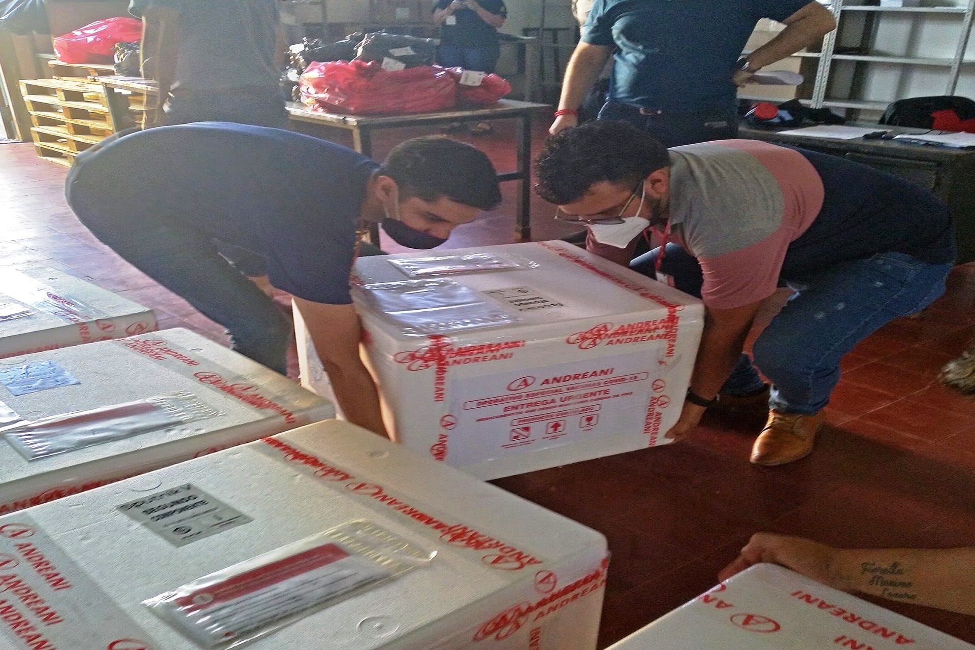 alt="dos personas descargan contenedores de la vacuna Sputnik V"