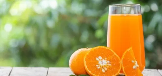 alt="en la imagen se ve una jarra con jugo de naranja, otra naranja cortada por la mitad y una naranja entera"