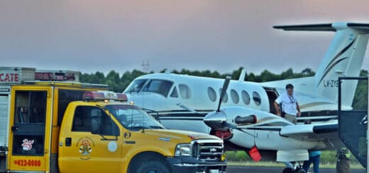 alt="vista parcial de un avión y una autobomba de los Bomberos Voluntarios, un hombre desciende por la escalerilla del avión"