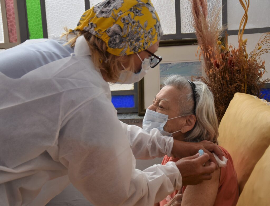 alt="una mujer con cabello blanco recibe una vacuna"