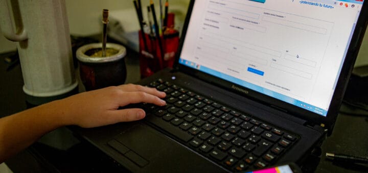 alt="pantalla de computadora portátil junto a un mate y la mano de quién está operando con ella"