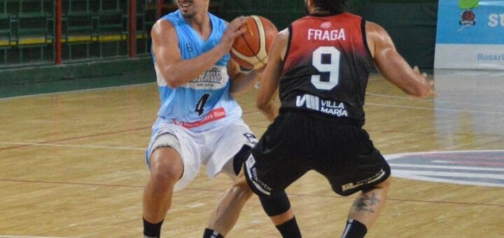 alt="un jugador de básquet, de frente en la fotografía, tiene entre sus manos el balón ante la marca de otro con una camiseta con el número 9, que está de espaldas"