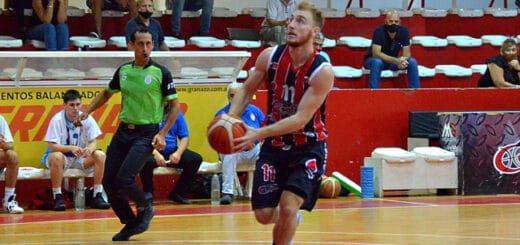 alt="en la fotografía, un jugador de central entrerriano encara el aro adversario, lo observa un árbitro, los suplentes y el público"