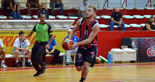 alt="en la fotografía, un jugador de central entrerriano encara el aro adversario, lo observa un árbitro, los suplentes y el público"