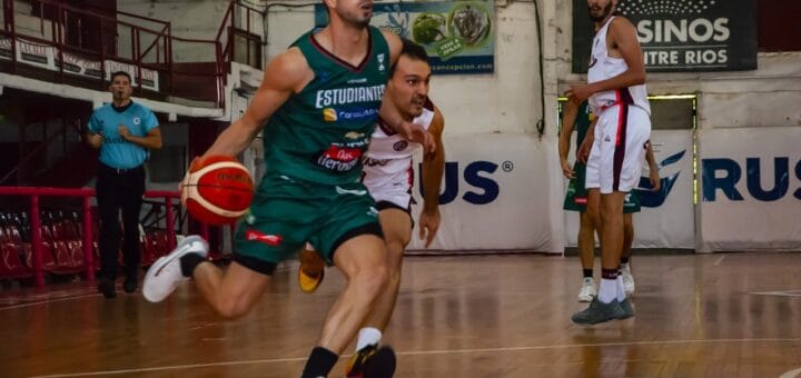 alt="un jugador de básquet corre con la pelota y es perseguido por otro, un tercero los mira"