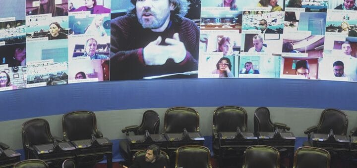 alt="panel con diputados participando virtualmente de la sesión en que se trató el impuesto a las ganancias, también pueden verse bancas vacías y un solo legislador que está presente"