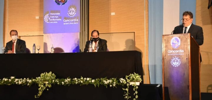 alt="el intendente de Concordia en una tarima, sentados detrás el presidente del Concejo Deliberante y el gobernador de Entre Ríos"