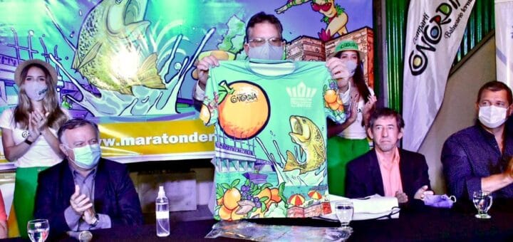 alt="parado, el intendente de concordia presenta la camiseta del maratón de reyes; sentados, tres funcionarios municipales"