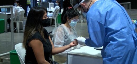 alt="una mujer con barbijo es asistida por dos trabajadores de la salud"