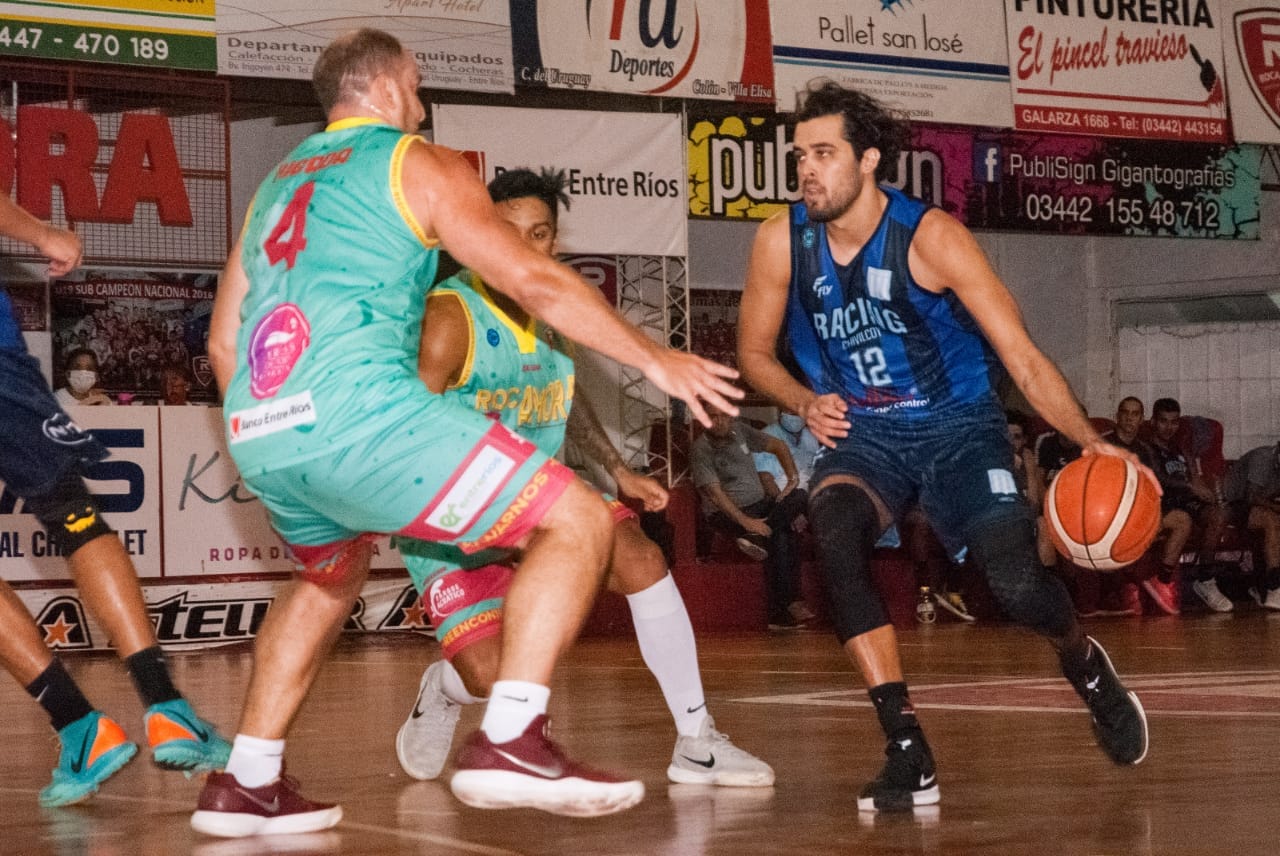 alt="un jugador de básquet pica el balón frente a dos rivales"