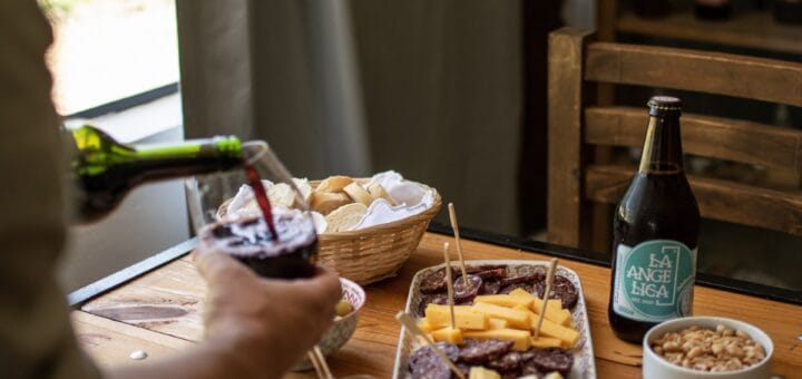 alt="mesa con una picada y vino, a la izquierda dos manos sirven una copa de vino"