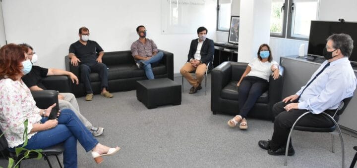 alt="en la fotografía hay siete personas reunidas en una sala, sentadas en sillas y sillones"