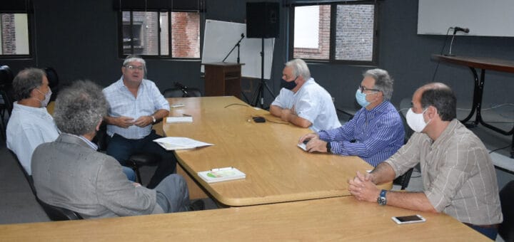 alt="en la imagen, seis hombre reunidos alrededor de una mesa con forma de L"