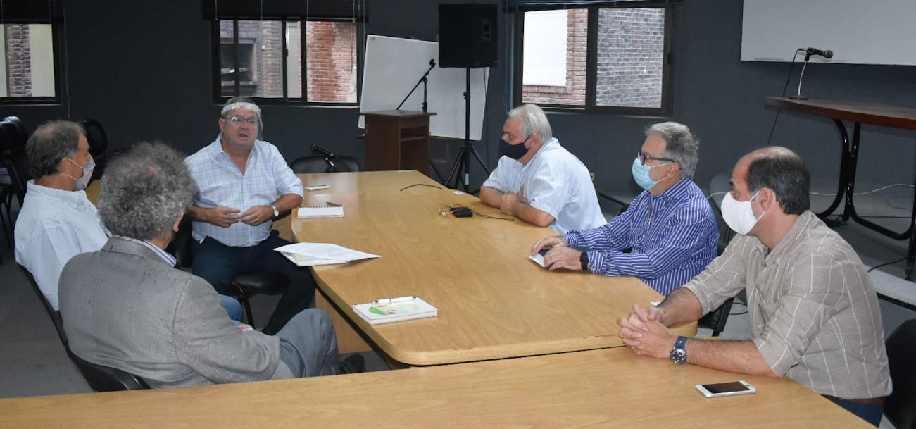 alt="en la imagen, seis hombre reunidos alrededor de una mesa con forma de L"