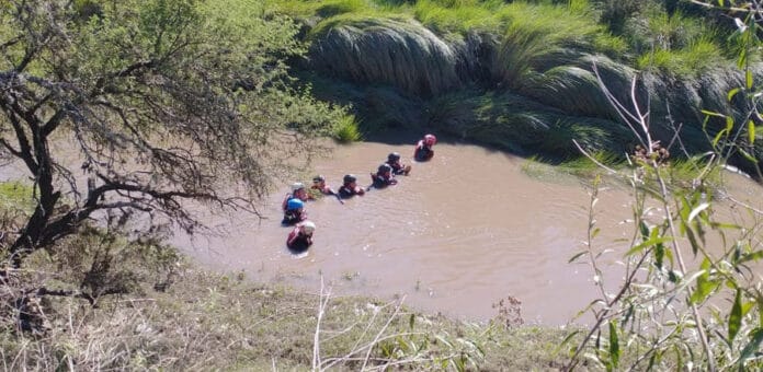alt="bomberos asegurados a una soga realizan un rastrillaje en un arroyo"
