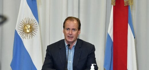 alt="el gobernador Bordet habla flanqueado por una bandera argentina a la izquierda y una entrerriana a la derecha, sobre una mesa un frasco de alcohol en gel"