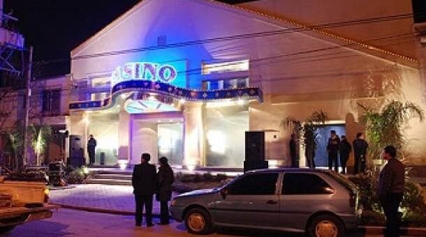alt="en la fotografía, el frente de un inmueble con un letrero luminoso que dice casino, en la calle algunas personas y un auto"