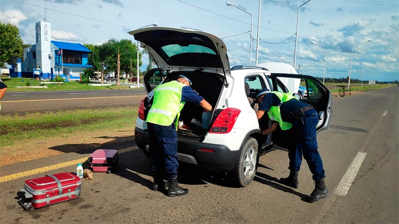 alt="dos policías inspeccionan un automóvil de color blanco, el vehículo tiene el capó, el baúl y las puertas abiertas; en el pavimento hay dos valijas"
