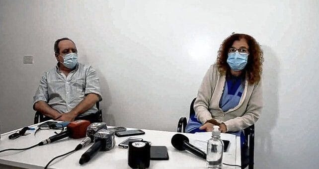 alt="en primer plano, micrófonos de radio y televisión sobre una mesa, detrás de la mesa, sentados, un hombre y una mujer"