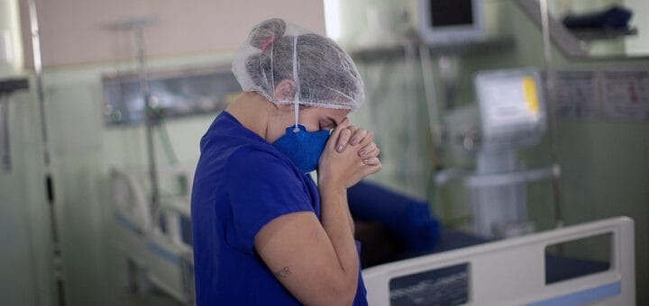 alt="una médica junta las manos en oración en una sala de terapia intensiva"