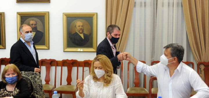 alt="a la derecha de la fotografía, el ministro de economía saluda con los puños a un gremialista, hay otros sindicalistas sentados en una mesa, mientras el ministro y otro hombre caminan detrás de ellos"