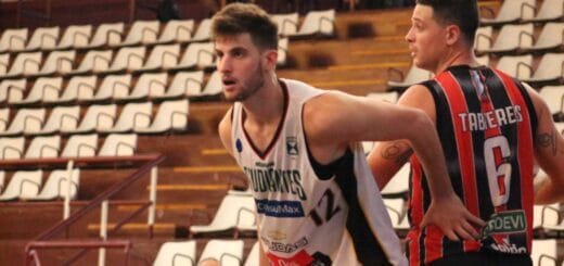 alt="en la fotografía, dos jugadores de básquet de equipos rivales, detrás de ellos las tribunas vacías"