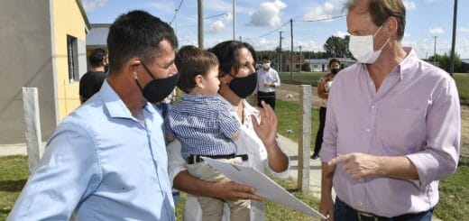alt="a la izquierda de la fotografía, una mujer con un niño en brazos y un papel en una mano, a su lado un hombre; a la derecha de la fotografía, el gobernador de Entre Ríos habla con la pareja"