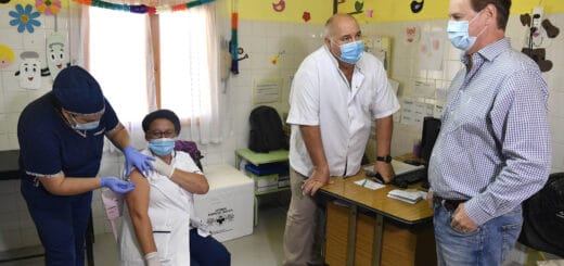 alt="a la izquierda, una enfermera aplica una vacuna a una mujer, a la derecha está el gobernador y un médico"