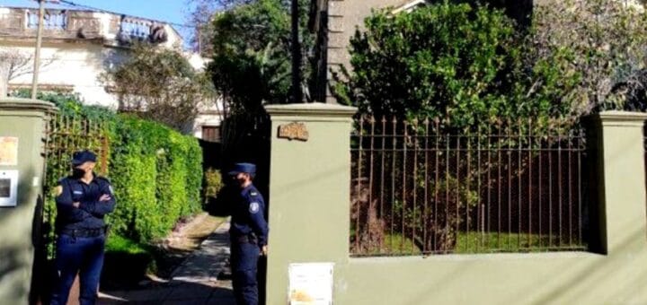 alt="dos policías hacen guardia en el portón de acceso a una vivienda"