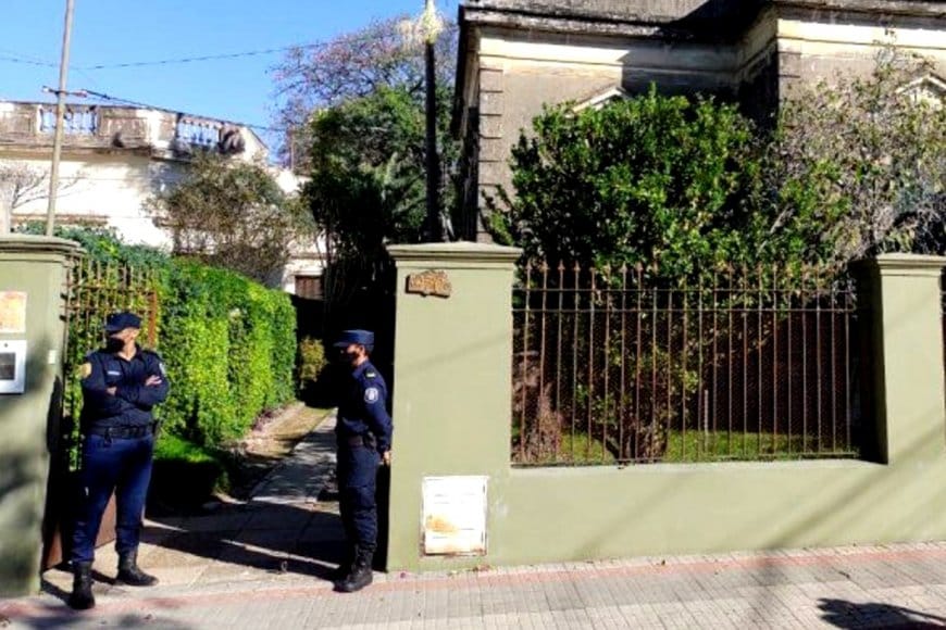 alt="dos policías hacen guardia en el portón de acceso a una vivienda"