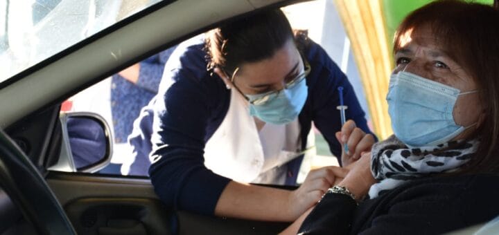alt="en la imagen, una mujer recibe una vacuna en el interior de su automóvil, otra mujer es quien se la aplica"