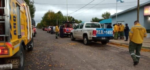 alt="vehículos de bomberos y de la policía estacionados en los dos lados de la calle; en la vereda, integrantes de la policía y de bomberos frente a una comisaría"