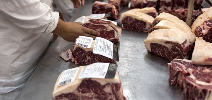 alt="manos de operarios de un frigorífico acomodan cortes de carne"