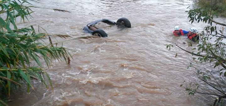 alt="en la imagen se ven dos ruedas de un automóvil sobresaliendo de un curso de agua"