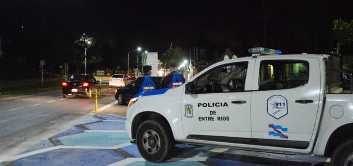 alt="en la imagen puede verse en primer plano una camioneta policial y adelante de ella, hacia el costado derecho, dos policías"