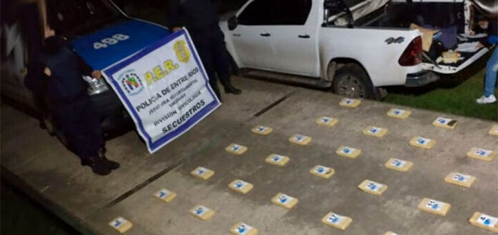 alt="en la fotografía puede verse en el ángulo superior izquierdo a dos policías, entre ambos una patrulla de cuyo capó cuelga un lienzo con la leyenda PER policía de entre ríos secuestros; en la zona central de la foto y hacia el ángulo inferior derecho varios paquetes conteniendo droga; en la parte superior y hacia la derecha hay una camioneta de color blanco"