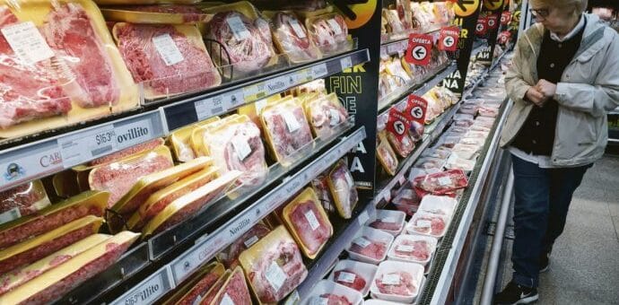 alt="en la imagen se ve a una mujer eligiendo cortes de carne vacuna en una góndola de supermercado"