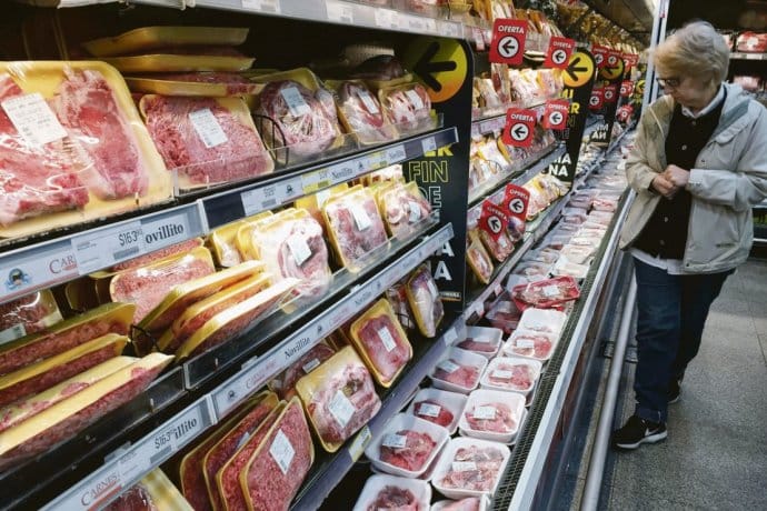 alt="en la imagen se ve a una mujer eligiendo cortes de carne vacuna en una góndola de supermercado"